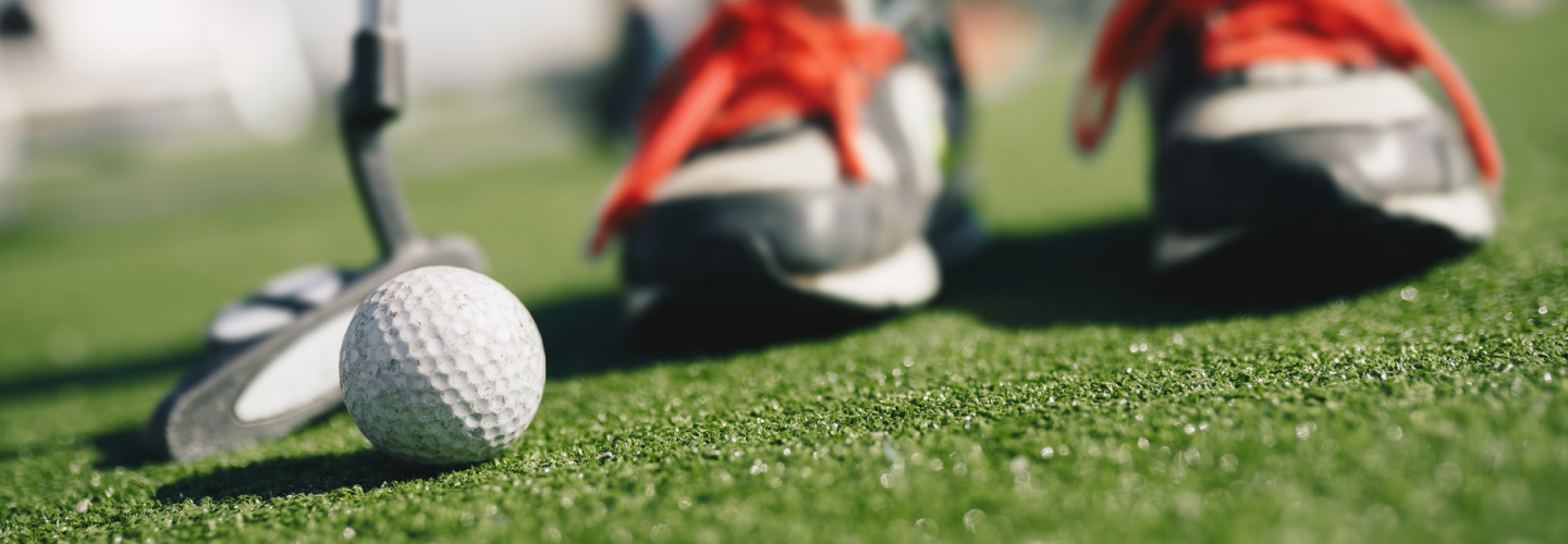 Golfboll på gräs med golfklubbor i bakgrunden