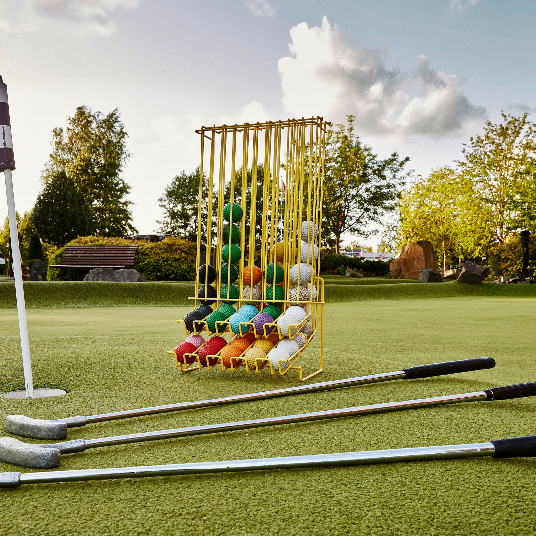 Minigolfklubbor och färgglada golfbollar i ställ på en konstgräsgreen en solig dag, redo för spel.